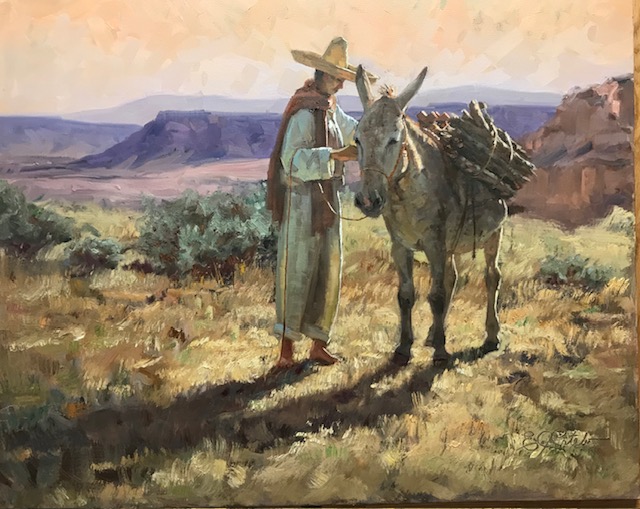 Man standing beside a burro loaded with firewood in a sunlit desert canyon