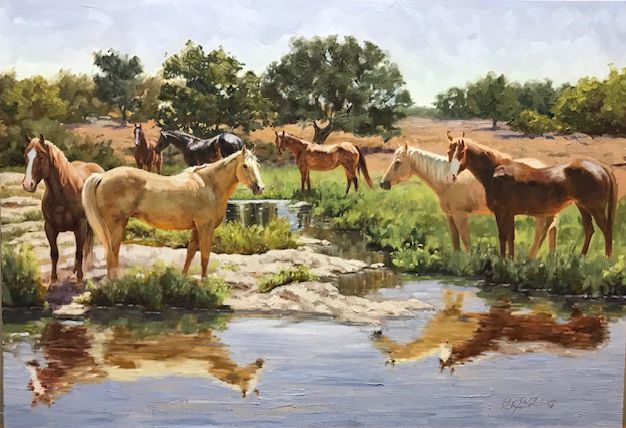 Group of horses gathered beside a creek with their reflections visible in the water