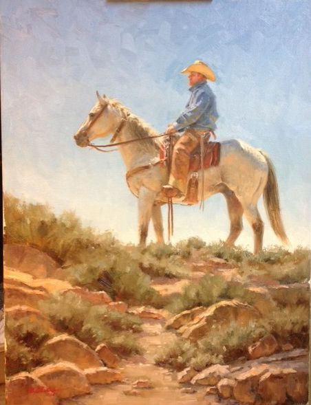 Cowboy seated on a light-colored horse atop a rocky rise beneath a pale blue sky